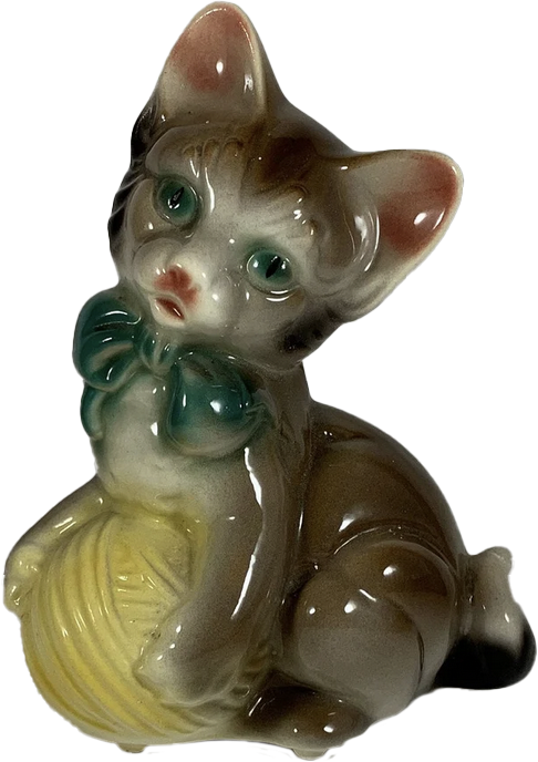 a porcelain statuette of a cat with a green bow standing on a ball of yellow yarn